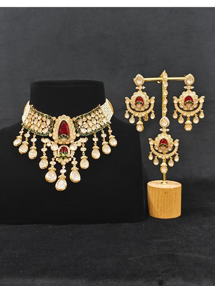 Close-up of an ornate traditional (Bright Gold) Red and Green Choker jewellery set and earrings and maangtikka with Uncut Kundan, American Diamond, Green Colored Stones, Pearls and Doublet Stone. Bride showcasing a premium imitation Moissanite jewelry set for her reception look. Wedding celebration styling with a luxury artificial Moissanite jewelry Set design.