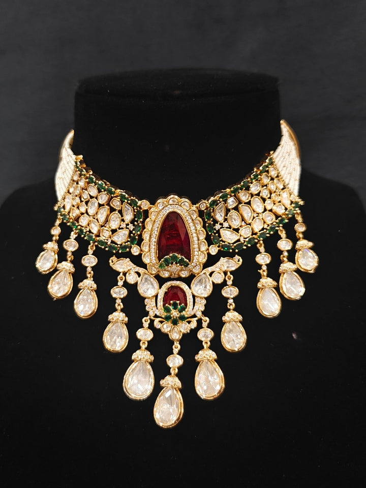 Close-up of an ornate traditional (Bright Gold) Red and Green Choker jewellery set and earrings and maangtikka with Uncut Kundan, American Diamond, Green Colored Stones, Pearls and Doublet Stone. Bride showcasing a premium imitation Moissanite jewelry set for her reception look. Wedding celebration styling with a luxury artificial Moissanite jewelry Set design.