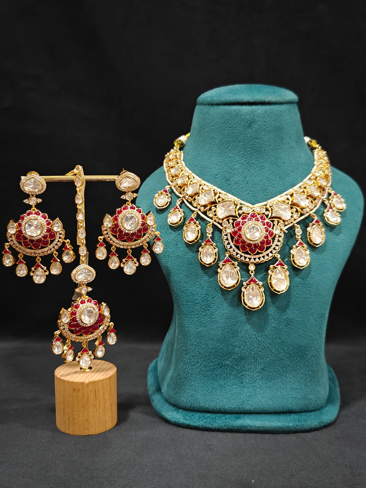 Close-up of an ornate traditional (Bright Gold) Red Collar jewellery set and earrings and maangtikka with Red Colored Stones, American Diamond, Pearls and Moissanite. Reception night styling featuring sparkling imitation Moissanite jewelry Set. Bride wearing a high-quality artificial Moissanite jewelry set for wedding rituals.