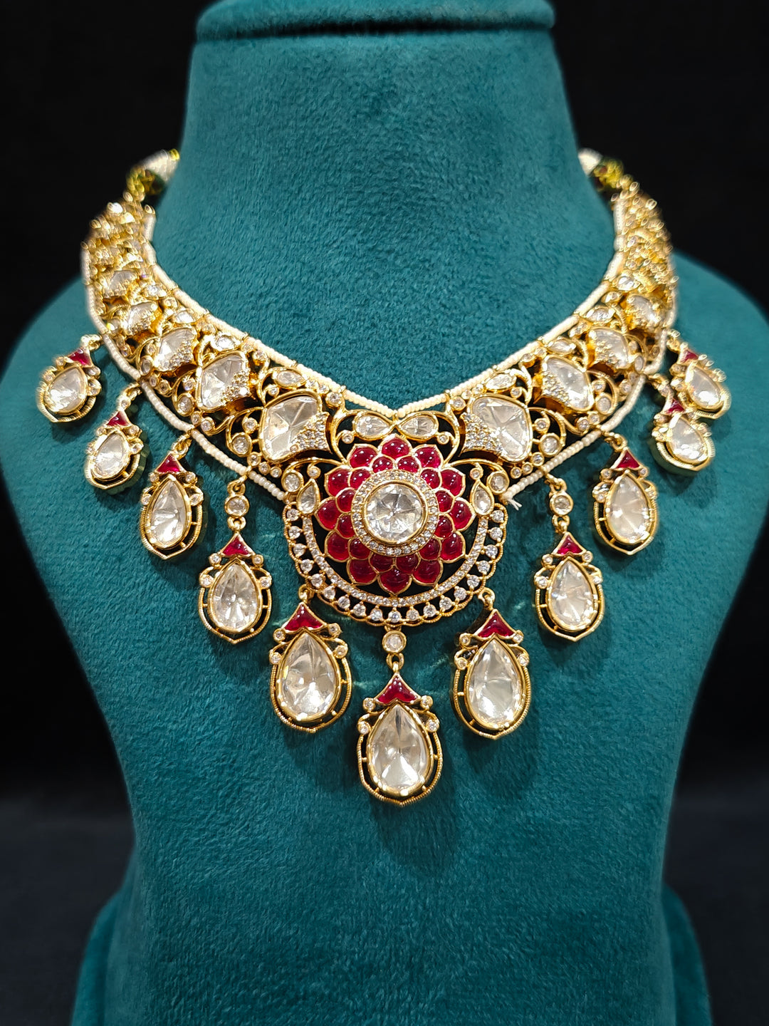 Close-up of an ornate traditional (Bright Gold) Red Collar jewellery set and earrings and maangtikka with Red Colored Stones, American Diamond, Pearls and Moissanite. Reception night styling featuring sparkling imitation Moissanite jewelry Set. Bride wearing a high-quality artificial Moissanite jewelry set for wedding rituals.