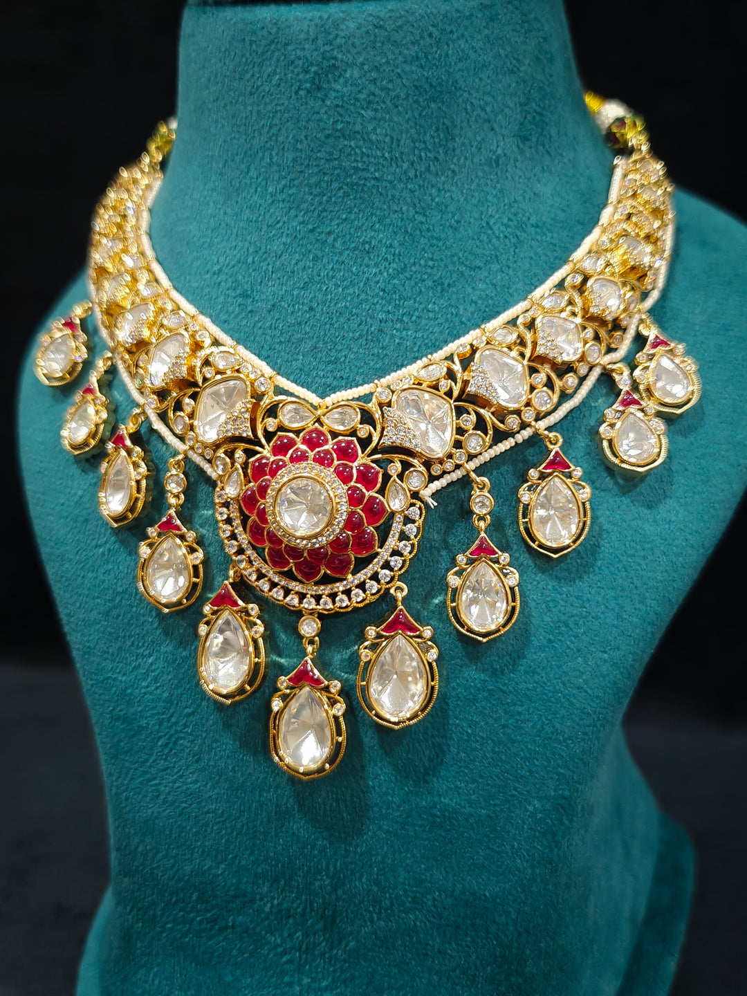 Close-up of an ornate traditional (Bright Gold) Red Collar jewellery set and earrings and maangtikka with Red Colored Stones, American Diamond, Pearls and Moissanite. Reception night styling featuring sparkling imitation Moissanite jewelry Set. Bride wearing a high-quality artificial Moissanite jewelry set for wedding rituals.