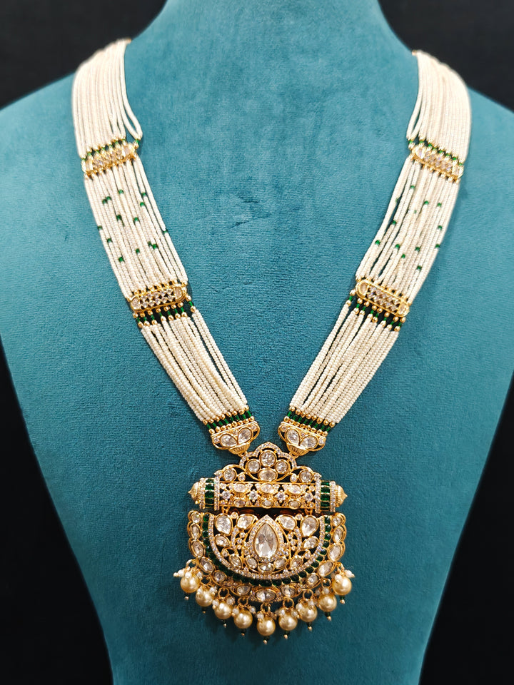 Close-up of an ornate traditional (Bright Gold) Green long jewellery set and earrings with Moissanite Polki, American Diamond, Green Colored Stones, Pearls, Beads and Hydro Crystals. Woman wearing Long artificial Moissanite jewelry for a grand celebration. Bride wearing a high-quality artificial Moissanite jewelry set for wedding rituals.