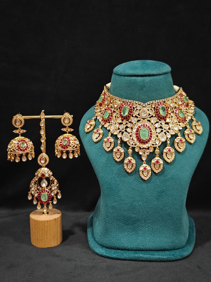 Close-up of an ornate traditional (Bright Gold) Mint Green and Ruby Pink Choker jewellery set and earrings and maangtikka with Doublet Stone, Moissanite, Kundan, American Diamond and Ruby Pink & Mint Green colored Stone. Bridal photoshoot look styled with a luxury imitation Moissanite jewelry set. Bride showcasing a traditional yet modern artificial Moissanite jewelry set design.