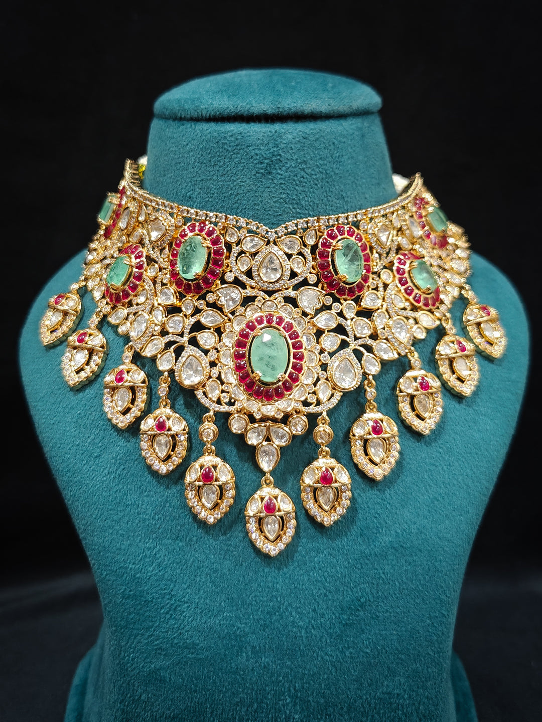 Close-up of a woman wearing an ornate traditional (Bright Gold) Mint Green and Ruby Pink Choker jewellery set and earrings and maangtikka with Doublet Stone, Moissanite, Kundan, American Diamond and Ruby Pink & Mint Green colored Stone. Bridal photoshoot look styled with a luxury imitation Moissanite jewelry set. Bride showcasing a traditional yet modern artificial Moissanite jewelry set design.