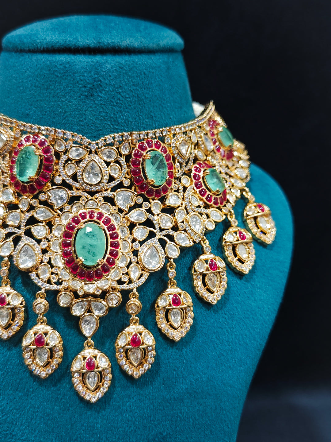 Close-up of an ornate traditional (Bright Gold) Mint Green and Ruby Pink Choker jewellery set and earrings and maangtikka with Doublet Stone, Moissanite, Kundan, American Diamond and Ruby Pink & Mint Green colored Stone. Bridal photoshoot look styled with a luxury imitation Moissanite jewelry set. Bride showcasing a traditional yet modern artificial Moissanite jewelry set design.