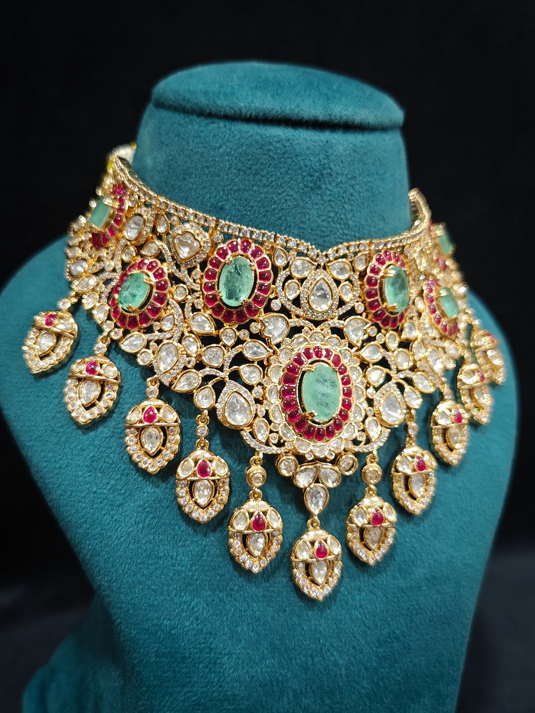 Close-up of an ornate traditional (Bright Gold) Mint Green and Ruby Pink Choker jewellery set and earrings and maangtikka with Doublet Stone, Moissanite, Kundan, American Diamond and Ruby Pink & Mint Green colored Stone. Bridal photoshoot look styled with a luxury imitation Moissanite jewelry set. Bride showcasing a traditional yet modern artificial Moissanite jewelry set design.
