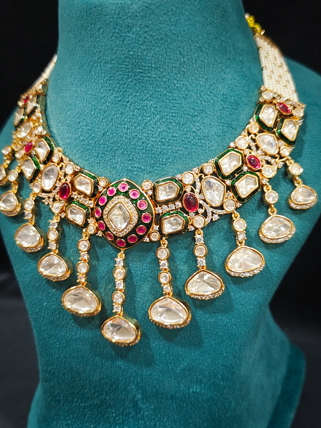 Close-up of an ornate traditional Meenakari Green and Pink Collar jewellery set and earrings and maangtikka with Pink Colored Stones, Uncut Kundan, American Diamond and Meenakari. Close-up of intricate Meenakari detailing in imitation bridal jewelry. Royal Indian bridal styling featuring a handcrafted Meenakari set.
