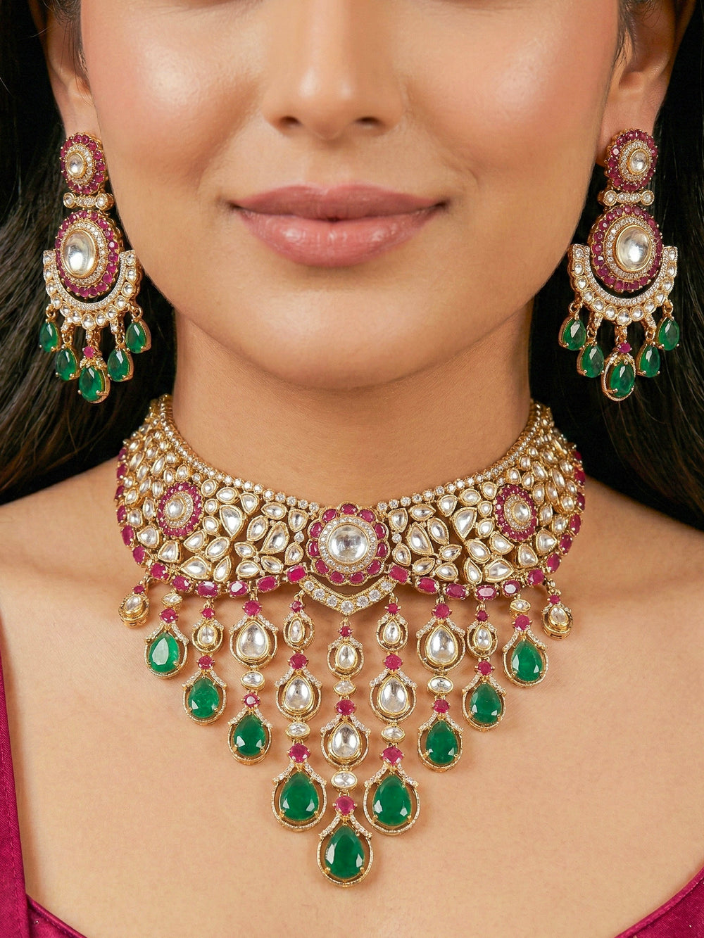 Close-up of a woman wearing an ornate traditional (Bright Gold) Ruby Pink and Green Collar jewellery set and earrings and maangtikka with Pink & Green Colored Stones, Kundan, Moissanite and American Diamond. Close-up of intricate detailing in high-quality artificial wedding Moissanite jewelry. Woman wearing a luxury artificial Moissanite jewelry set styled for an Indian wedding celebration.