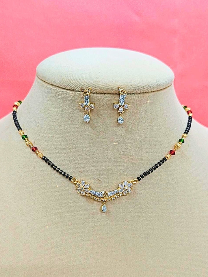 Tina Mangalsutra—a gold necklace with black mangalsutra beads and matching earrings, pendant featuring sparkling American Diamonds—set against a cream dummy, perfect for your wedding ceremony dress. Diamond mangalsutra. Modern mangalsutra. 