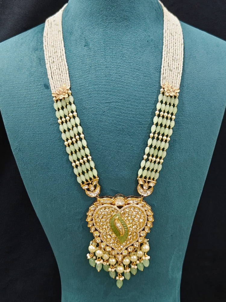Close-up of an ornate traditional (Gold Polish) Mint Green Long jewellery set and earrings with Polki, American Diamond Tumble Beads and Pearls. Woman wearing trending Polki artificial jewelry for the wedding season in India. Wedding guest outfit styled with an elegant Polki necklace set.