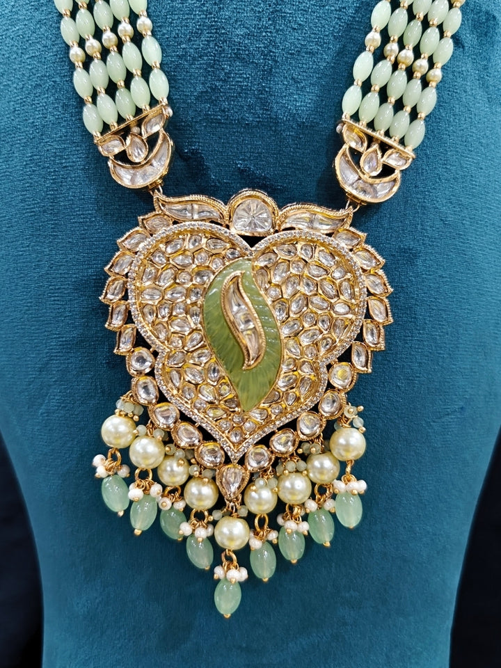 Close-up of an ornate traditional (Gold Polish) Mint Green Long jewellery set and earrings with Polki, American Diamond Tumble Beads and Pearls. Woman wearing trending Polki artificial jewelry for the wedding season in India. Wedding guest outfit styled with an elegant Polki necklace set.