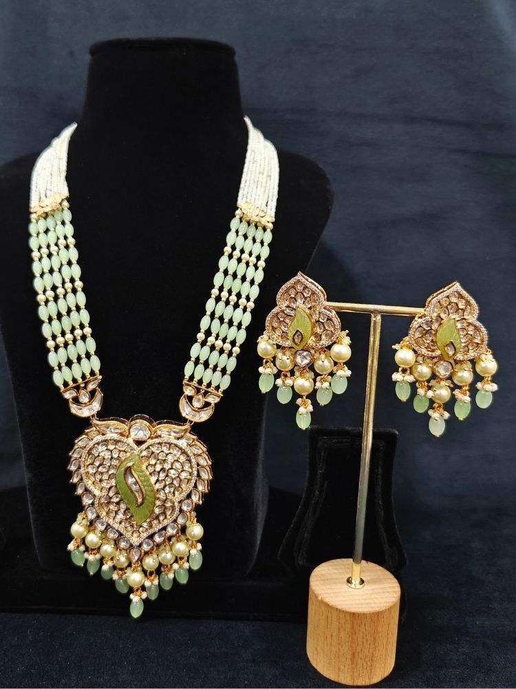 Close-up of an ornate traditional (Gold Polish) Mint Green Long jewellery set and earrings with Polki, American Diamond Tumble Beads and Pearls. Woman wearing trending Polki artificial jewelry for the wedding season in India. Wedding guest outfit styled with an elegant Polki necklace set.