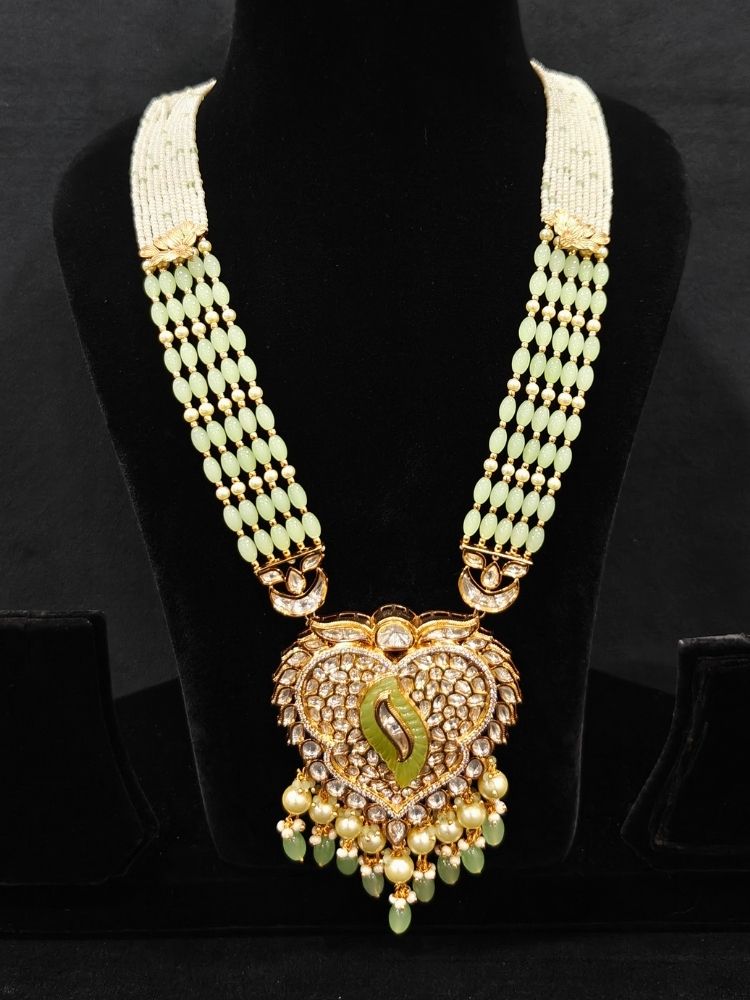 Close-up of an ornate traditional (Gold Polish) Mint Green Long jewellery set and earrings with Polki, American Diamond Tumble Beads and Pearls. Woman wearing trending Polki artificial jewelry for the wedding season in India. Wedding guest outfit styled with an elegant Polki necklace set.