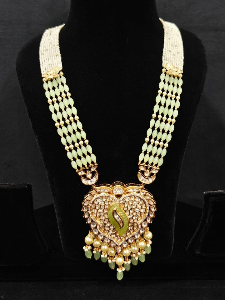 Close-up of an ornate traditional (Gold Polish) Mint Green Long jewellery set and earrings with Polki, American Diamond Tumble Beads and Pearls. Woman wearing trending Polki artificial jewelry for the wedding season in India. Wedding guest outfit styled with an elegant Polki necklace set.