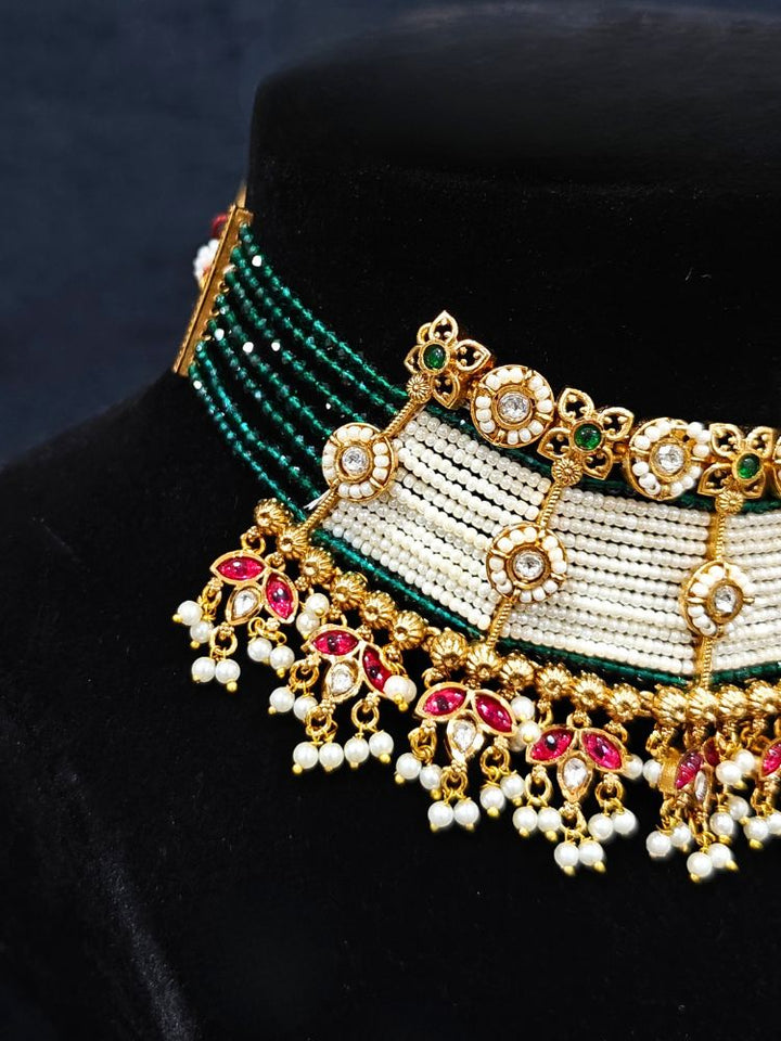 Close-up of an ornate traditional (Gold Polish) Choker White jewellery set and earrings with Pearl, Polki, Colored Stones, and crystal Beads. Woman wearing trending Polki artificial jewelry for the wedding season in India. Festive celebration look completed with premium imitation Polki jewelry.