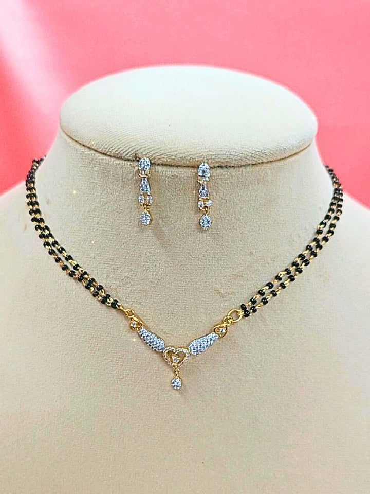  Urvashi Mangalsutra—a gold necklace with black mangalsutra beads and matching earrings, pendant featuring sparkling American Diamonds—set against a cream dummy, perfect for your wedding ceremony dress. Diamond mangalsutra. Modern mangalsutra. 