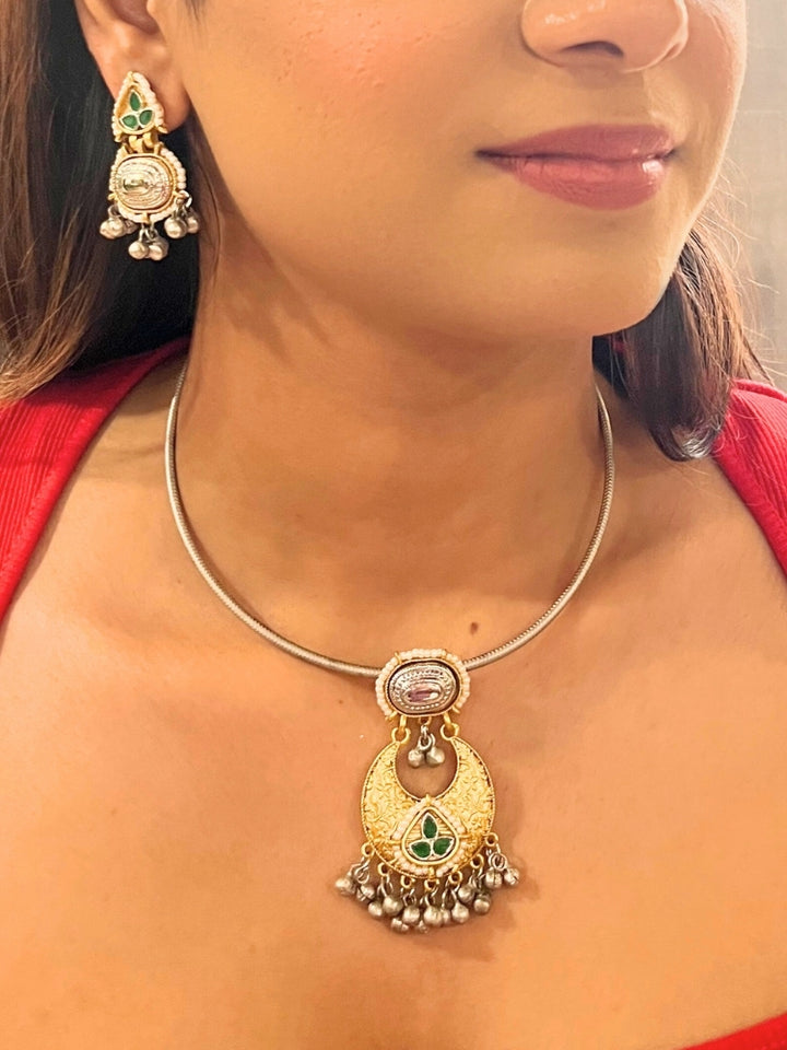 A woman wears the Usha Green Necklace Set, featuring colored stones and matching earrings. The brass pendant oxidized necklace pops against her red top, with just her lower face, neck, and upper chest in view.