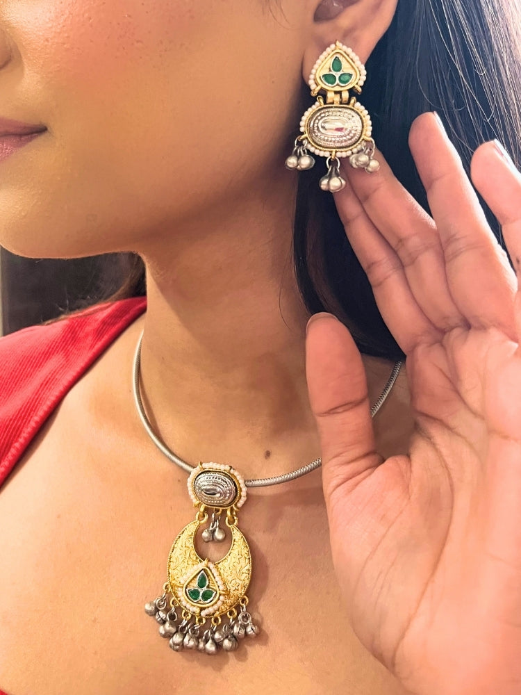 A woman wears the Usha Green Necklace Set, featuring colored stones and matching earrings. The brass pendant oxidized necklace pops against her red top, with just her lower face, neck, and upper chest in view