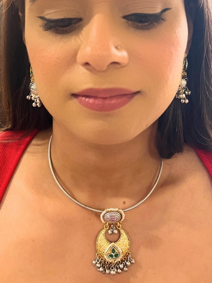 A woman wears the Usha Green Necklace Set, featuring colored stones and matching earrings. The brass pendant oxidized necklace pops against her red top, with just her lower face, neck, and upper chest in view