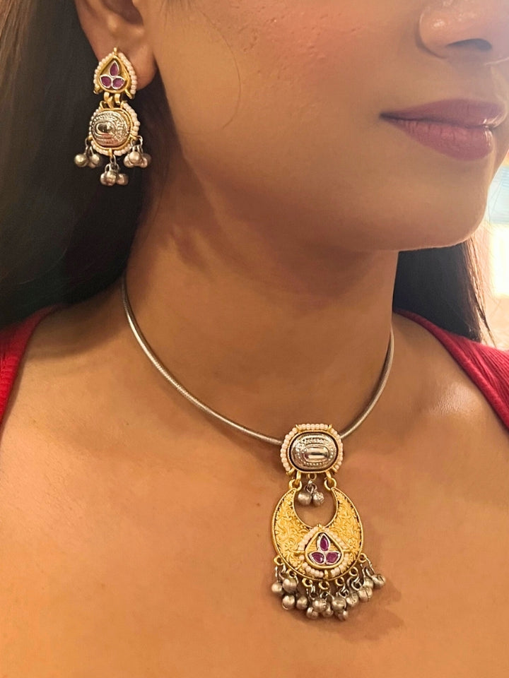 A woman wears the Usha Pink Necklace Set, featuring colored stones and matching earrings. The brass pendant oxidized necklace pops against her red top, with just her lower face, neck, and upper chest in view