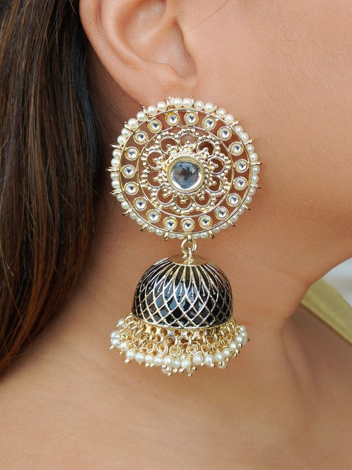 A close-up of a womans ear wearing Vanya Earrings, featuring Kundan work on the top round circle, a Jhumka in gold and black Meenakari work, adorned with small white beads.