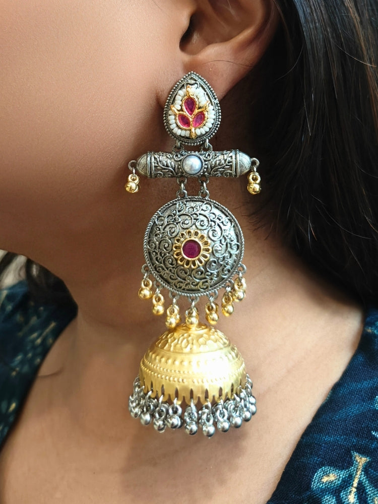 A close-up of a womans ear wearing Varnika Pink Earrings: ornate jhumkas with intricate silver and gold detailing, pink accents, and dangling golden beads—perfect for complementing a wedding ceremony dress. Long Oxidized earrings, german silver earrings, navratri earrings. 