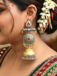A close-up of a womans ear wearing Varnika Pink Earrings: ornate jhumkas with intricate silver and gold detailing, pink accents, and dangling golden beads—perfect for complementing a wedding ceremony dress. Long Oxidized earrings, german silver earrings, navratri earrings. 