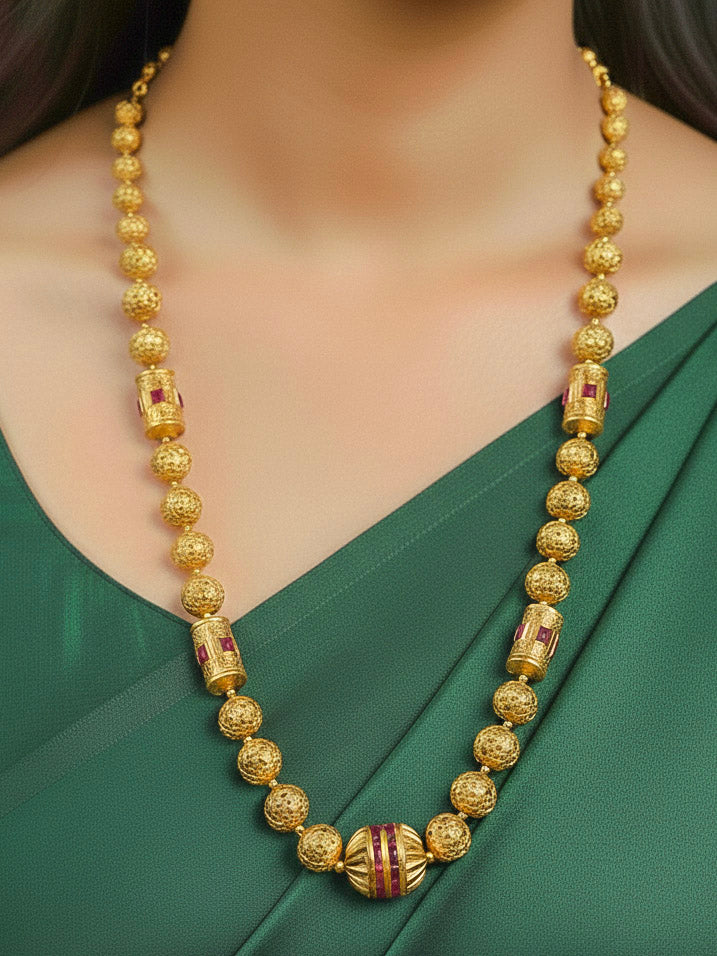 Close-up of a woman wearing an ornate traditional (Bright Gold Polish) Long Jewellery Set with Earrings with Ruby Red Colored Stones and Filigree Work. Saree look completed with an elegant Colored Stone artificial jewelry piece. Woman wearing trending Colored Stone artificial jewelry for wedding season in India.