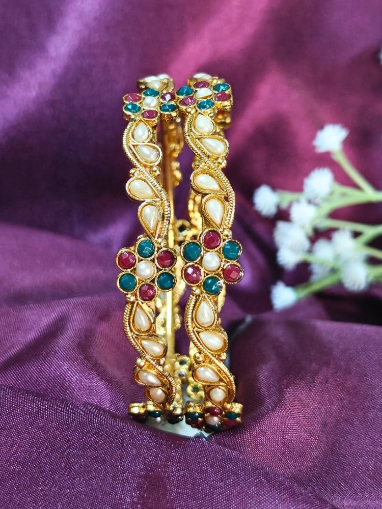 Close-up of an ornate traditional (Gold Polish) Pearl Bangles Set with Red and Green Colored Stone and Pearls. Festive celebration look enhanced with statement artificial bangles. Woman wearing anti-tarnish artificial bangles for long functions.