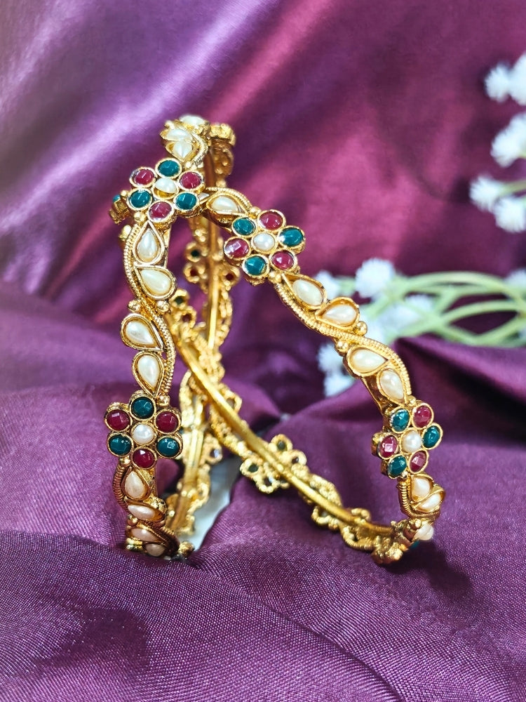 Close-up of an ornate traditional (Gold Polish) Pearl Bangles Set with Red and Green Colored Stone and Pearls. Festive celebration look enhanced with statement artificial bangles. Woman wearing anti-tarnish artificial bangles for long functions.
