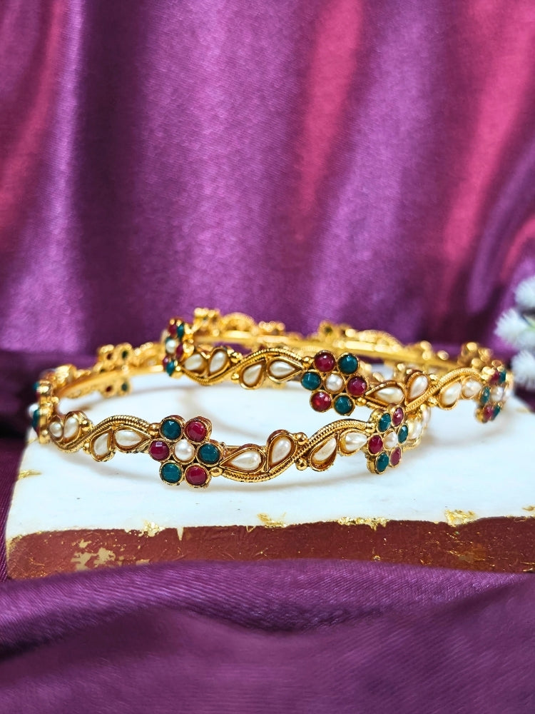 Close-up of an ornate traditional (Gold Polish) Pearl Bangles Set with Red and Green Colored Stone and Pearls. Festive celebration look enhanced with statement artificial bangles. Woman wearing anti-tarnish artificial bangles for long functions.