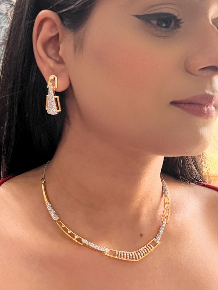 A woman, shown from the side and slightly smiling, wears the Vega Necklace Set featuring geometric American Diamonds gold and diamond-studded earrings with a matching Gold & White textured necklace—ideal for pairing with a cocktail gown.