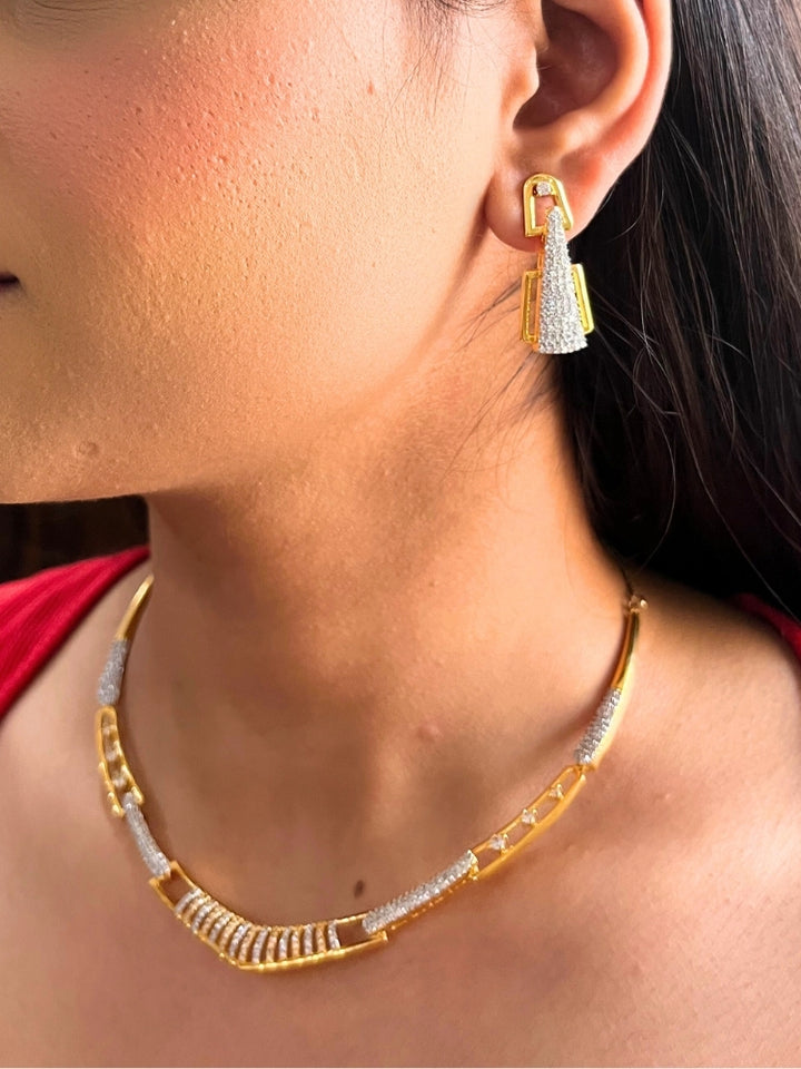 A woman, shown from the side and slightly smiling, wears the Vega Necklace Set featuring geometric American Diamonds gold and diamond-studded earrings with a matching Gold & White textured necklace—ideal for pairing with a cocktail gown.