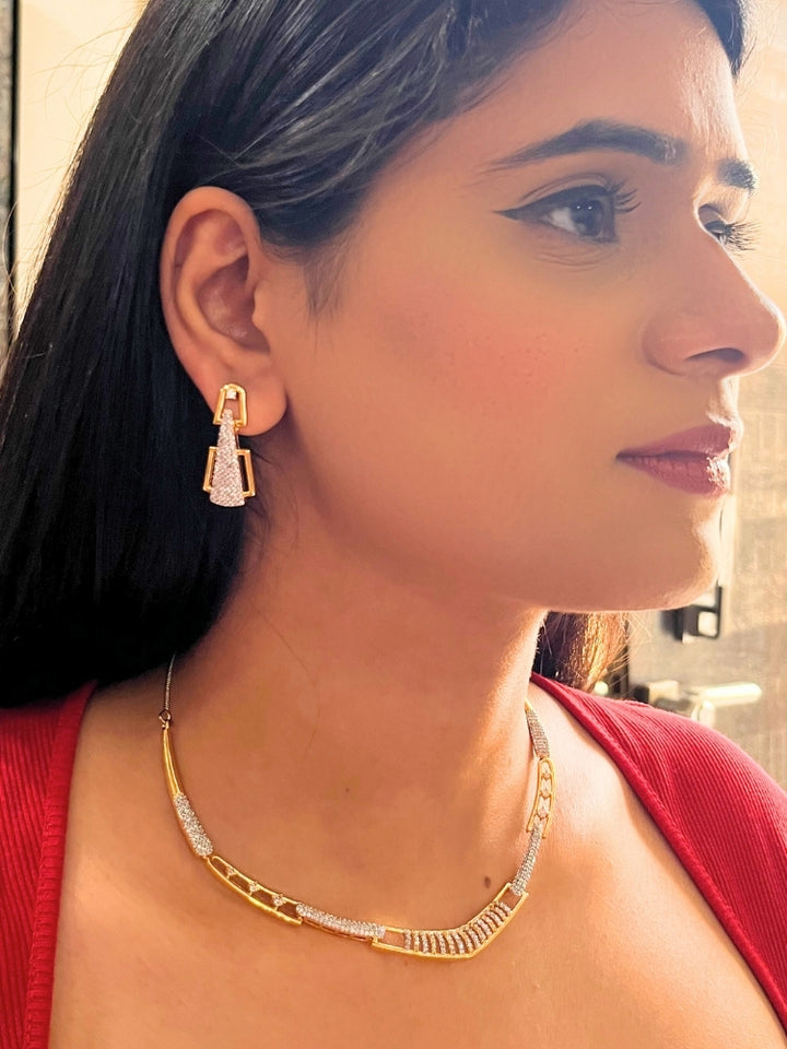 A woman, shown from the side and slightly smiling, wears the Vega Necklace Set featuring geometric American Diamonds gold and diamond-studded earrings with a matching Gold & White textured necklace—ideal for pairing with a cocktail gown.