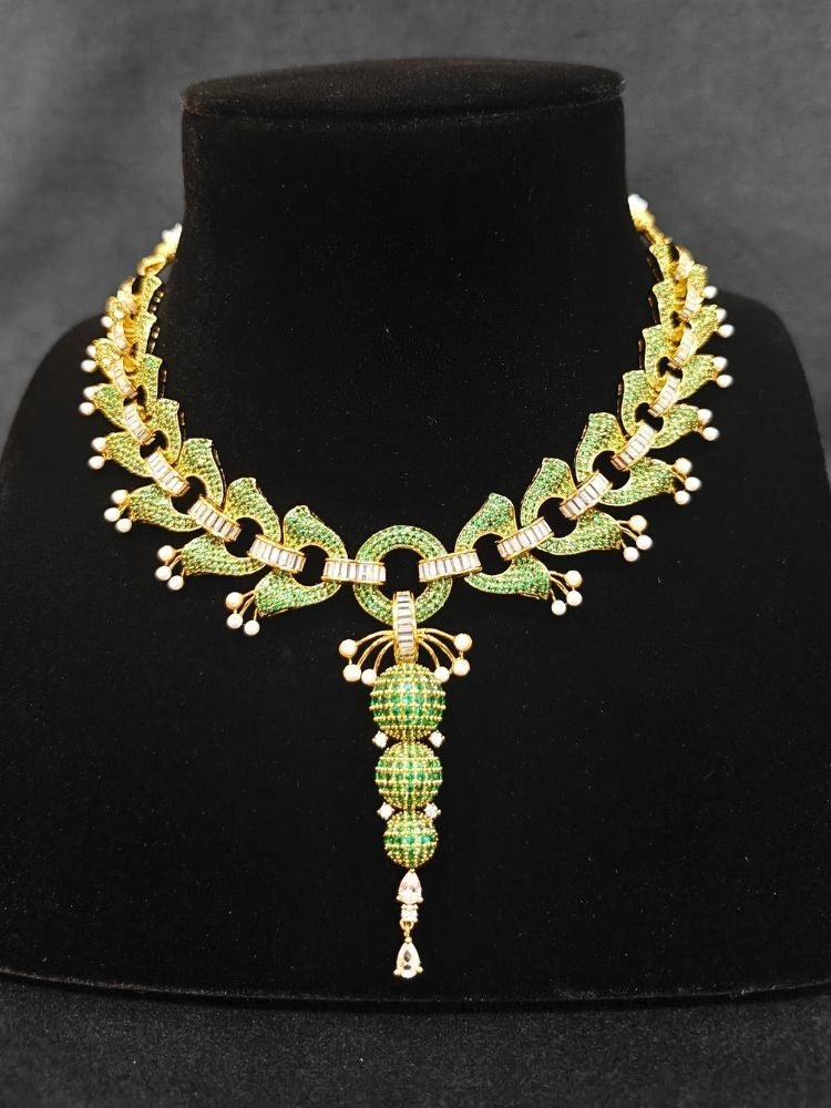 Close-up of an ornate Indo-Westerrn Green Collar jewellery set and earrings with Green Colored Stones, Baguette American Diamonds and Pearls. Reception party styling featuring a premium Colored Stones imitation set. Close-up of a cocktail party look featuring a premium Colored Stones necklace.