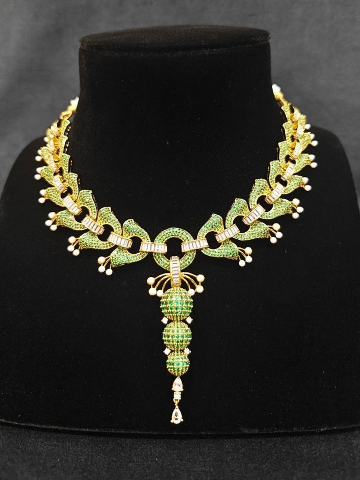 Close-up of an ornate Indo-Westerrn Green Collar jewellery set and earrings with Green Colored Stones, Baguette American Diamonds and Pearls. Reception party styling featuring a premium Colored Stones imitation set. Close-up of a cocktail party look featuring a premium Colored Stones necklace.