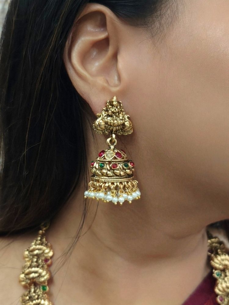 A woman in a maroon saree with gold embroidery and a cream blouse, adorned with traditional South-Indian jewelry, including the Vibhuti Temple Necklace Set featuring an ornate Laxmi necklace and matching temple jhumka earrings.