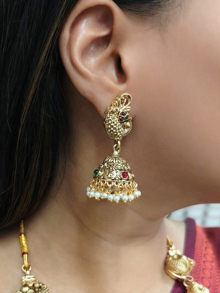 A woman wearing a maroon and teal silk saree, gold earrings, and the Vidya Temple Necklace Set—a grand gold necklace with intricate designs and pearl accents—perfect for a wedding ceremony.  Perfect necklace to add to your temple necklace collection. 