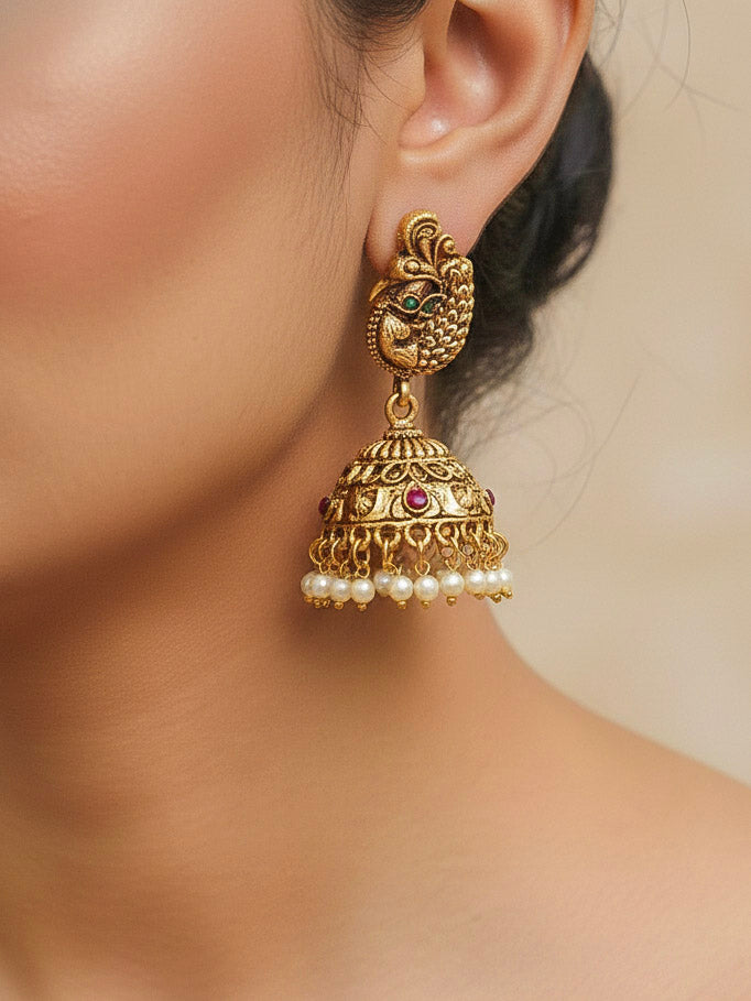 A woman wearing the Vidya Temple Necklace Set featuring a traditional gold Long necklace and matching earrings with Goddess Laxmi in the middle, along with pink and green colored stones, Pearls and Mehendi Polish. Wedding guest look completed with a temple necklace set. Close-up of detailed temple carvings in artificial wedding jewelry.