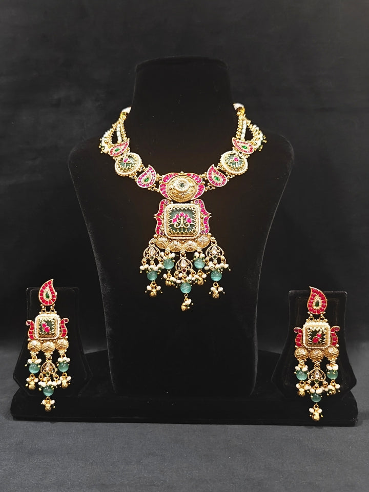 Close-up of an ornate traditional (Gold Polish) Pink & Mint Green Collar jewellery set and earrings and with Enamel and Pearls. Wedding celebration look featuring a premium heritage artificial set. Woman wearing a heritage-style artificial necklace for long wedding functions.