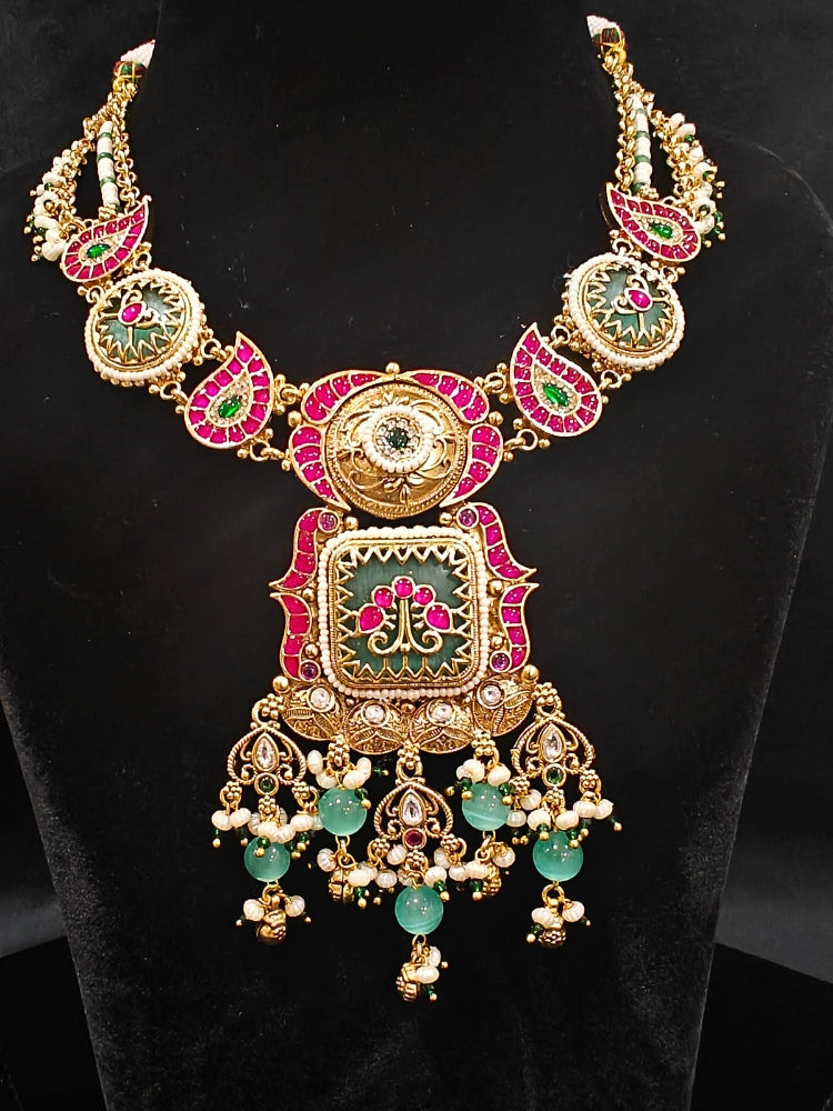 Close-up of an ornate traditional (Gold Polish) Pink & Mint Green Collar jewellery set and earrings and with Enamel and Pearls. Wedding celebration look featuring a premium heritage artificial set. Woman wearing a heritage-style artificial necklace for long wedding functions.
