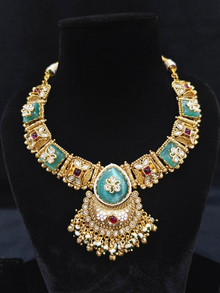 Close-up of an ornate traditional Mint Green Heritage gold Collar jewellery set and earrings with Mint Green Colored Stones, Kundan and Pearls. Woman styling a vintage heritage artificial necklace for a reception party. Perfect  Heritage necklace set for weddings and festivals.