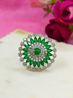 The Wallace Green Ring features a circular design with a central purple gemstone, surrounded by American diamonds and marquise-shaped Green stones, set against a Green and white background adorned with roses. Perfect American Diamond cocktail ring. 