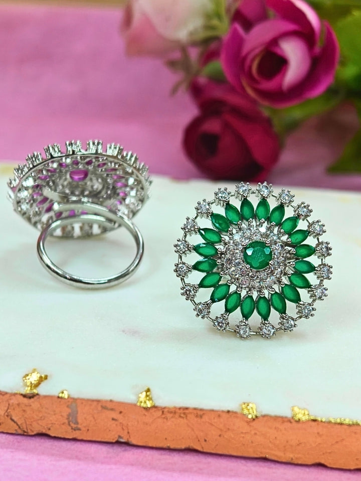 The Wallace Green Ring features a circular design with a central purple gemstone, surrounded by American diamonds and marquise-shaped Green stones, set against a Green and white background adorned with roses. Perfect American Diamond cocktail ring. 