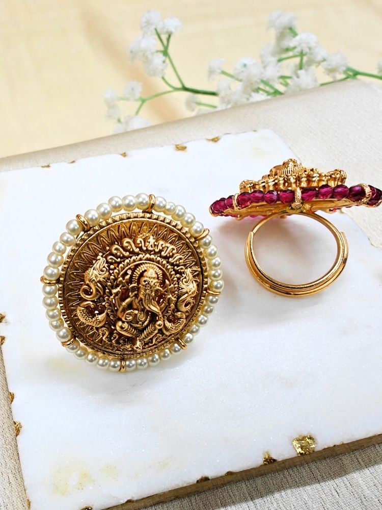 The White Bheema Ring is a round, gold-toned adjustable ring featuring Ganeshji made in intricate detailing at the center, encircled by Pearls. Displayed on white cloth with small flowers, its ideal for enhancing your wedding ceremony outfit.