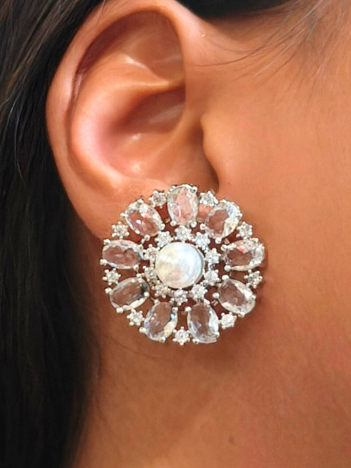 A close-up of a womans ear wearing the White Blossom stud Earrings—large, circular White earrings with a pearl at the center, colorful accents, and a border of sparkling American Diamonds. The stud earrings give a flower earrings feel. 