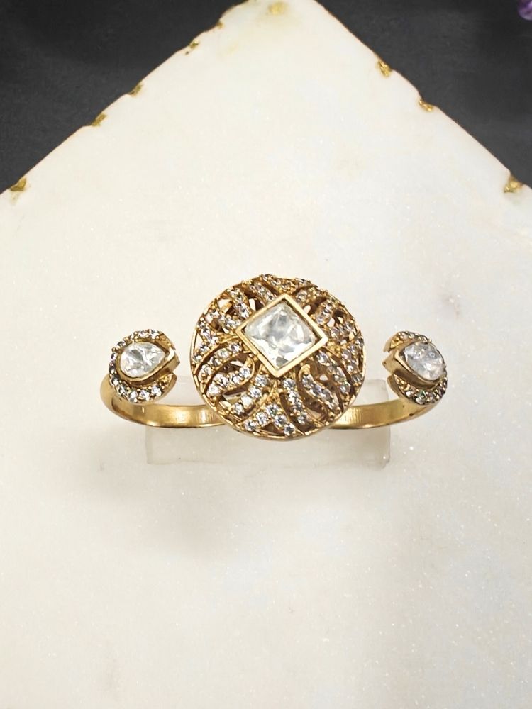 The White Octavia Ring features a gold band with a round, ornate centerpiece set with a clear American Diamond and two smaller White gemstones on the side, displayed on a white surface with gold trim. Multi-finger ring, great for cocktail parties. 