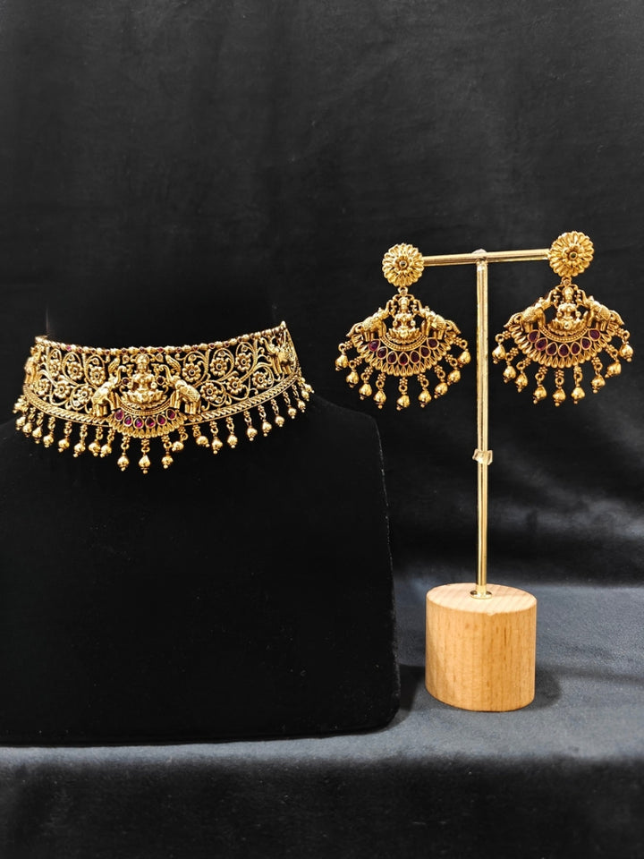 The Yagnika Choker Necklace Set featuring a traditional gold choker necklace and matching chandbali earrings with Goddess Laxmi in the middle, along with pink and green colored stones, golden elephants at the corners, paired with a pink and gold blouse—ideal party jewelry for any festive occasion.