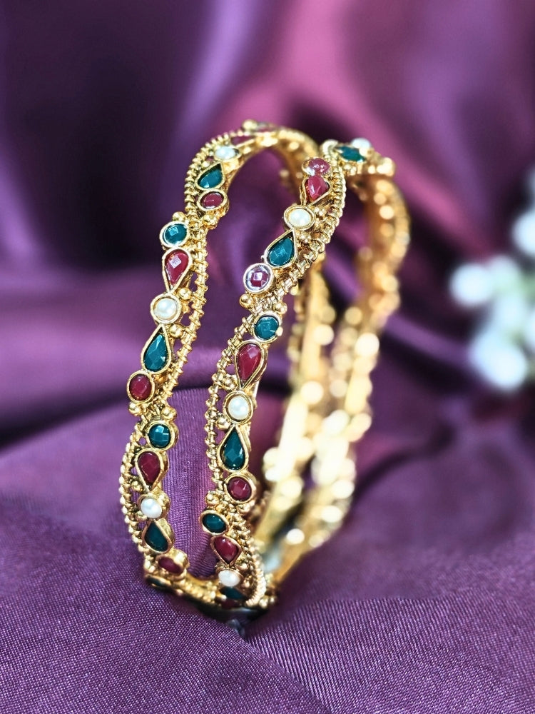Close-up of an ornate traditional (Gold Polish) Bangles Set with Red and Green Colored Stone. Festive Navratri outfit paired with stacked imitation Colored Stone bangles. Festive celebration look enhanced with artificial Colored Stone bangles.