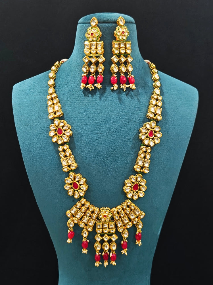 Close-up of an ornate traditional (Gold Polish) White Long jewellery set and earrings with Kundan, Red Colored Stone and Red Beads. Woman wearing trending Kundan artificial jewelry for wedding season in India. Wedding guest wearing a lightweight Kundan necklace for a festive function.